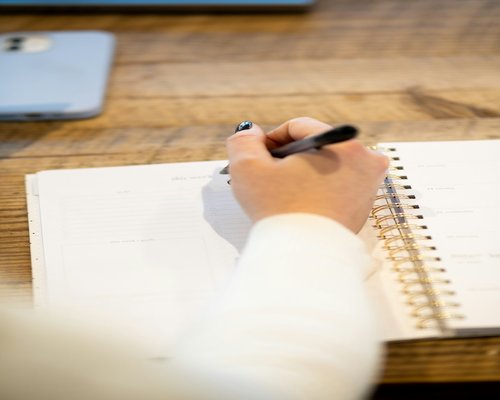 A close up of a person writing a daily plan in a notebook